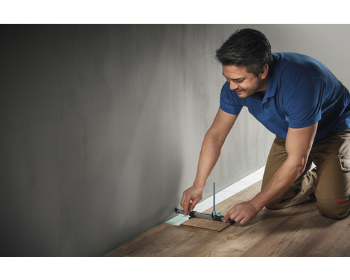 Ein Mann benutzt ein Anreißwerkzeug, um ein Laminatstück an einer Wand zu messen.