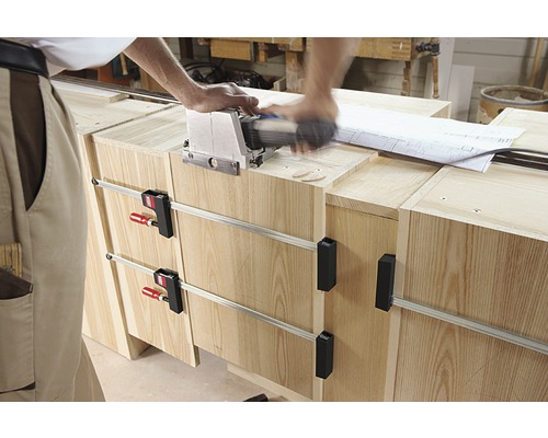 Handwerker arbeitet mit einer Lamellofräse an einem Holzmöbelstück, das mit Schraubzwingen fixiert ist.
