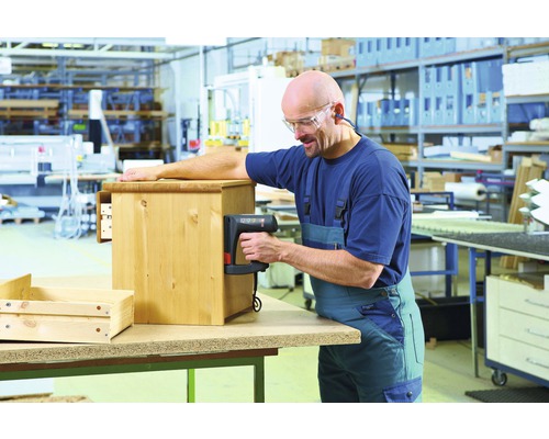 Ein Mann benutzt einen Tacker, um ein Holzmöbelstück in einer Werkstatt zusammenzubauen.