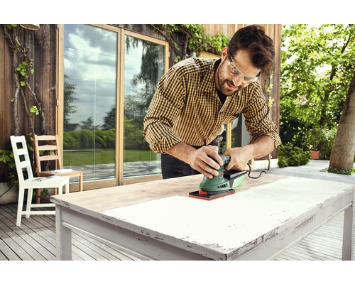Mann schleift Tischplatte im Aussenbereich mit einem Schleifgerät