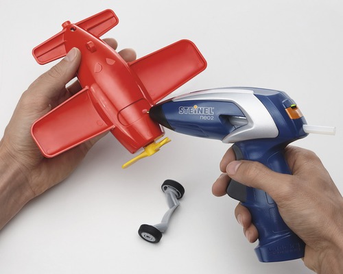 Person benutzt eine Heißklebepistole, um ein rotes Spielzeugflugzeug zu reparieren