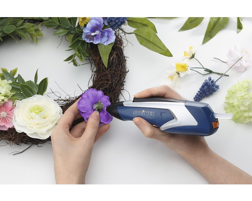 Frau befestigt Dekorationen mit einer Heißklebepistole an einem Kranz