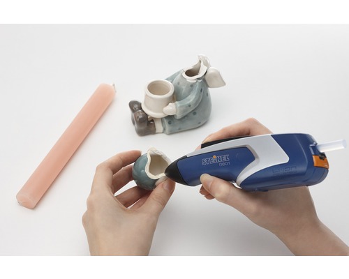 Person repariert eine Keramikfigur mit einer Heißklebepistole von Steinel.