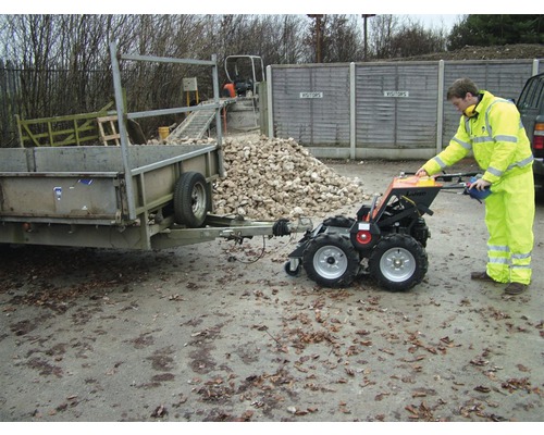 Person bedient einen Mini-Transporter, der einen Anhänger zieht. Im Hintergrund befindet sich ein Haufen Steine.