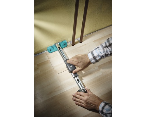 Person verlegt Laminat mit einem Zugeisen entlang einer Wand.