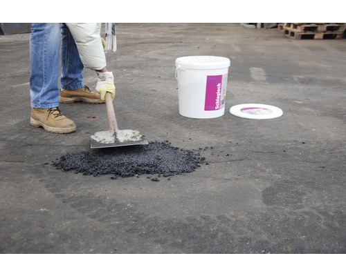 Verarbeitung von Schlagloch Reparaturmasse mit einer Schaufel neben einem Eimer.