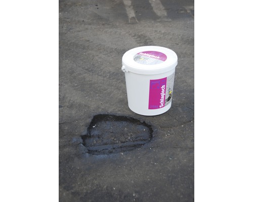 Eimer Schlagloch Reparaturmasse neben einem reparierten Schlagloch