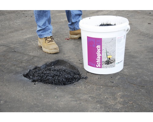 Ein Eimer Schlaglochreparaturmasse neben einem reparierten Schlagloch.