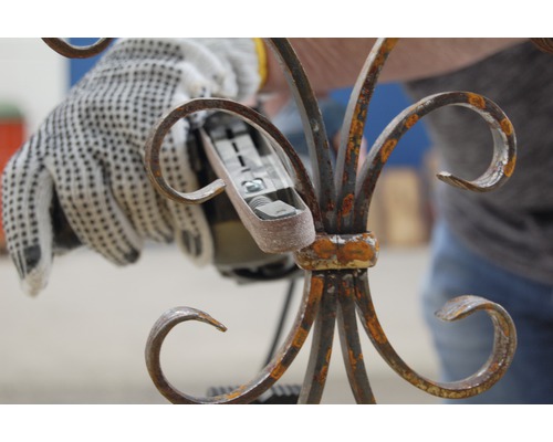 Eine Person verwendet einen Winkelschleifer an einem verzierten Metallstück.