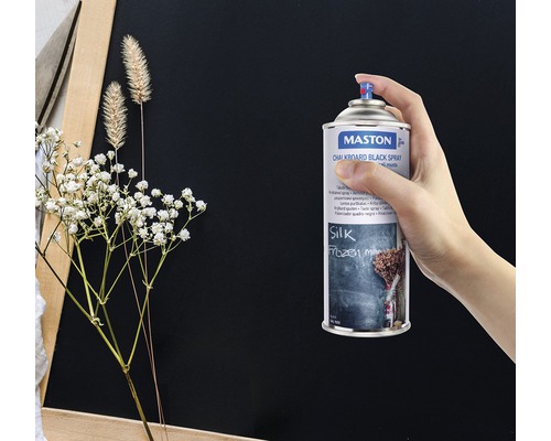 Eine Hand hält eine Dose Maston Tafellack Schwarz Spray vor einer Tafel.