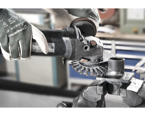 Eine Person benutzt eine Drahtbürste an einem Winkelschleifer zum Reinigen eines Metallteils, das in einem Schraubstock befestigt ist.