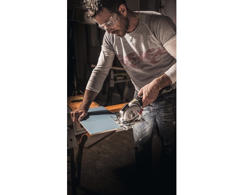 Ein Mann mit Schutzbrille schneidet eine Fliese mit einer Handkreissäge.