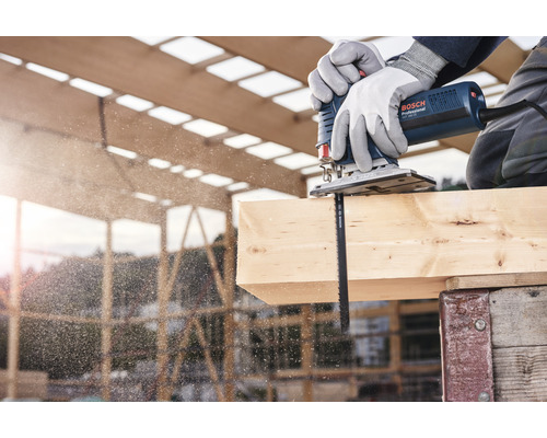 Eine Stichsäge schneidet ein Holzbrett, während ein Arbeiter Handschuhe trägt.