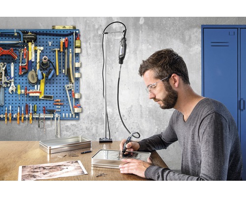 Mann graviert mit einem Dremel Werkzeug in eine Metallbox auf einem Schreibtisch, Werkzeugwand im Hintergrund