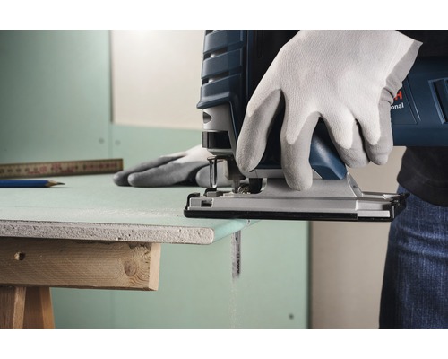 Nahaufnahme einer Stichsäge beim Schneiden einer Gipskartonplatte, bedient von einer Person mit Handschuhen.