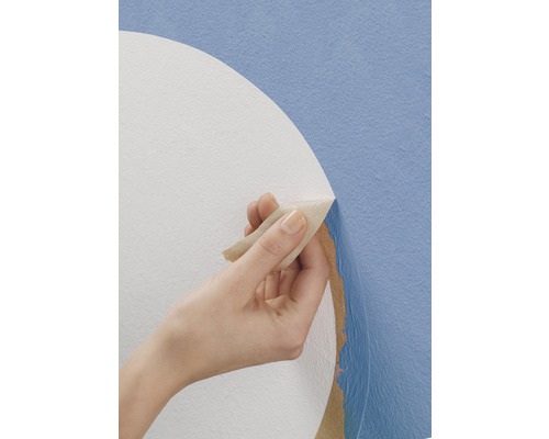 Eine Hand entfernt eine Tapete von einer Wand.