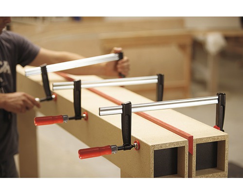 Mann befestigt Werkstück mit Schraubzwingen