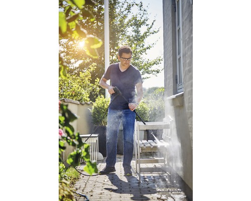 Eine Person reinigt eine Gartenbank mit einem Hochdruckreiniger im Freien.