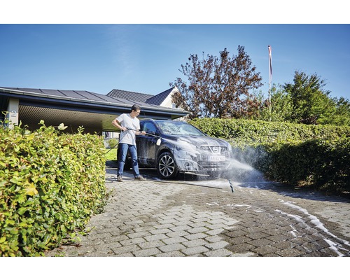 Eine Person reinigt ein Auto mit einem Hochdruckreiniger auf einer gepflasterten Auffahrt
