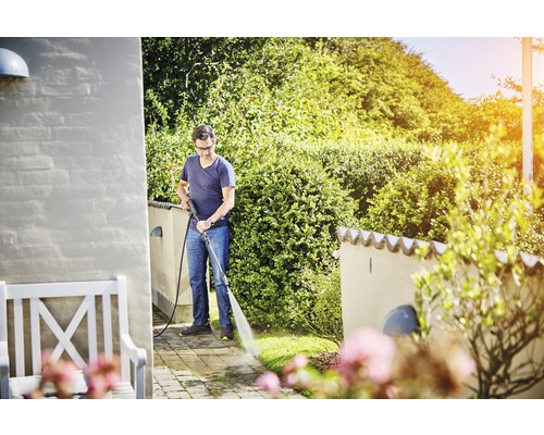 Ein Mann reinigt eine Terrasse mit einem Hochdruckreiniger im Garten.