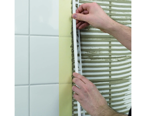 Ein Mann bringt eine Fliesenschiene an einer Wand mit Fliesen an.