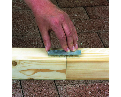 Eine Hand drückt eine Nagelplatte in ein Holzstück