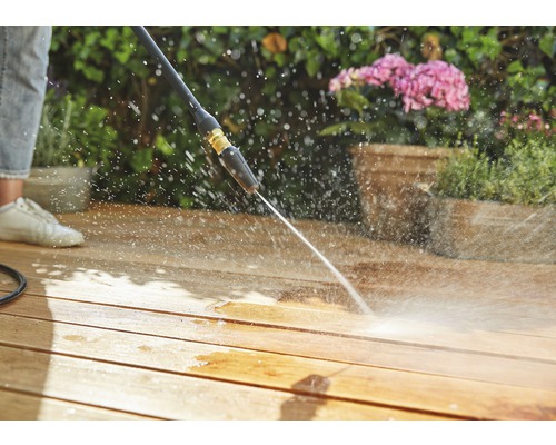 Eine Person reinigt eine Holzterrasse mit einem Hochdruckreiniger.