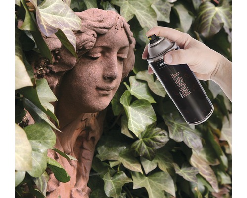 Eine Hand sprüht mit einer Rosteffekt-Sprühfarbe auf eine Steinstatue vor einem Efeuhintergrund.