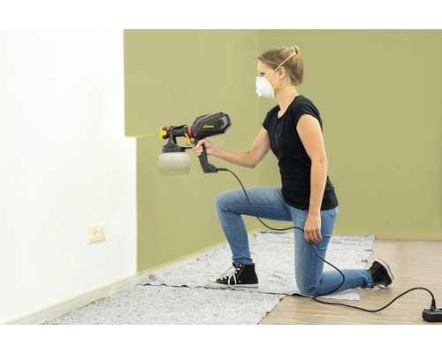 Frau verwendet eine Farbspritzpistole zum Streichen einer Wand.