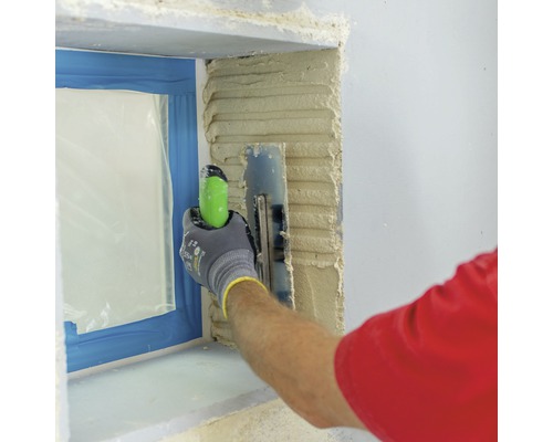 Ein Mann trägt mit einer Zahnspachtel Putz auf eine Fensterlaibung auf