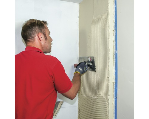 Ein Mann trägt Fliesenkleber mit einer Kelle auf eine Wand auf