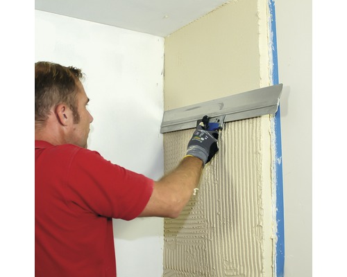 Ein Mann glättet Putz mit einer Glättkelle an einer Wand. Das Bild zeigt die Anwendung von Putz im Innenbereich.