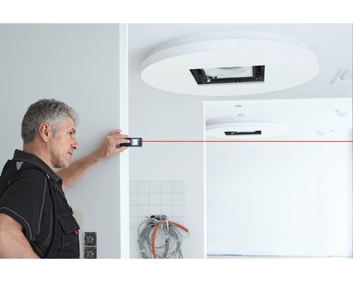 Handwerker misst mit Laser-Distanzmessgerät einen Raum.