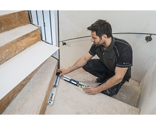 Ein Handwerker misst mit einem Winkelmesser eine Treppe. Bosch Logo