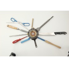 Anordnung verschiedener Werkzeuge um eine Schleifscheibe: Schere, Stecheisen, Bohrer, Schraubendreher, Spachtel, Messer und Drechselwerkzeug.
