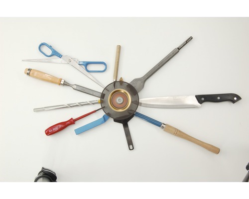 Anordnung verschiedener Werkzeuge um eine Schleifscheibe: Schere, Stecheisen, Bohrer, Schraubendreher, Spachtel, Messer und Drechselwerkzeug.
