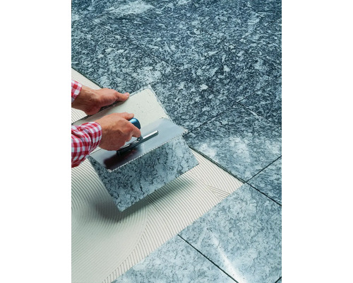 Verlegen von grauen Bodenfliesen mit Spachtel und Fliesenkleber