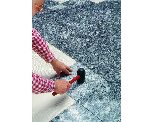 Ein Mann verlegt Steinzeugfliesen mit einem Gummihammer