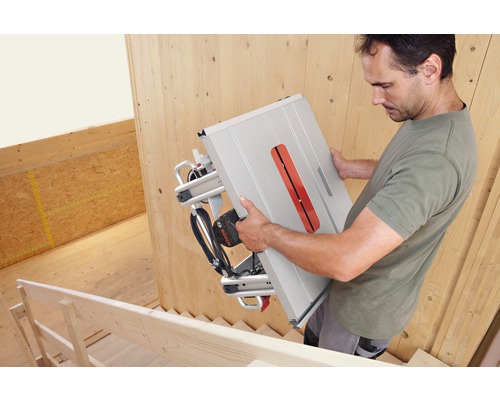 Ein Mann trägt eine Bosch Tischkreissäge auf einer Treppe.