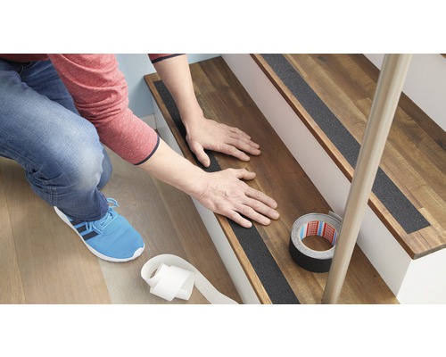 Person befestigt Antirutschstreifen auf einer Holztreppe.