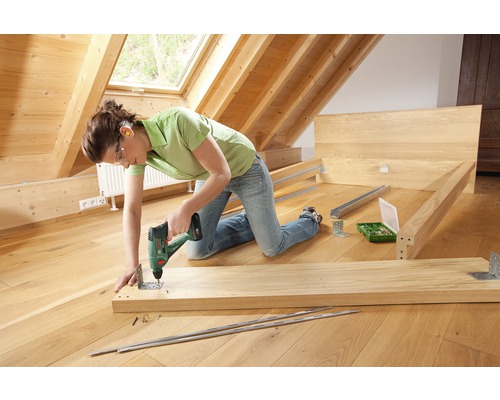 Eine Person montiert ein Holzbett mit einem Akkuschrauber.