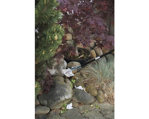 Szene mit einem Müllgreifer, der Papier in einem Garten mit Steinen und Pflanzen aufhebt