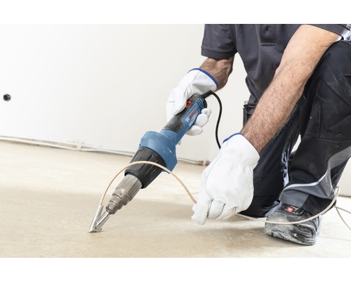 Handwerker bearbeitet Boden mit Heissluftfön der Marke Bosch