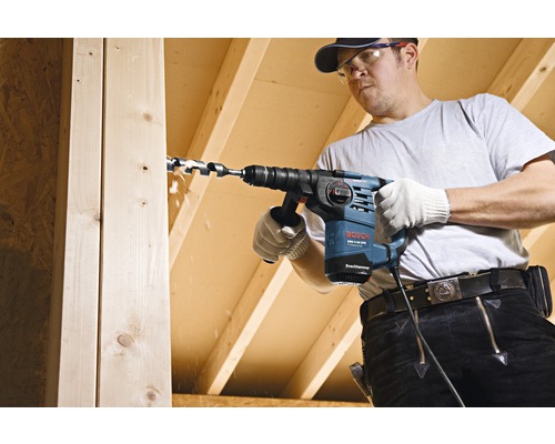 Handwerker bohrt mit einer Bosch Bohrmaschine ein Loch in ein Holzbrett.