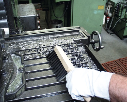 Eine Person reinigt eine Werkbank mit einer Bürste von Metallspänen.