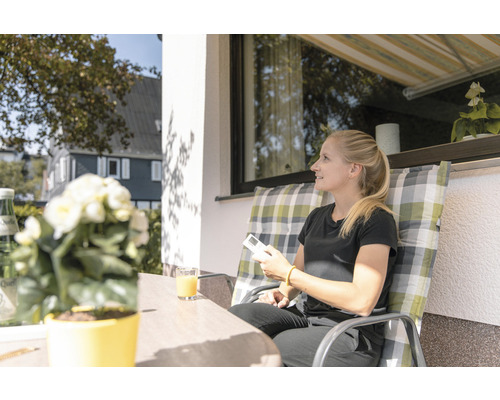Frau sitzt auf der Terrasse unter einer Markise und bedient eine Fernbedienung.