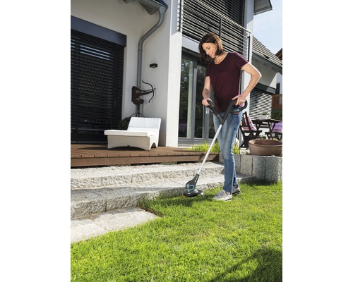 Frau benutzt einen Rasentrimmer im Garten.