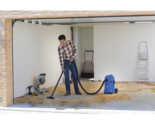 Mann saugt Späne mit einem Nass Trockensauger in einer Garage auf.