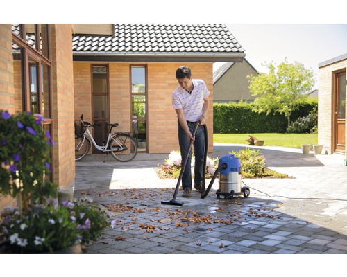 Mann reinigt mit einem Nass Trockensauger eine gepflasterte Fläche im Freien von Blättern.
