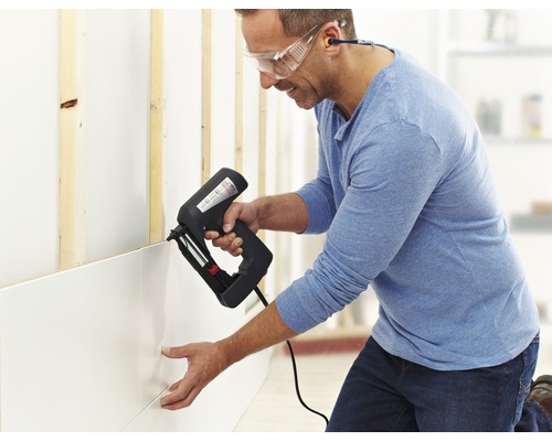 Ein Mann befestigt mit einem Elektrotacker Wandpaneele an einer Wand.